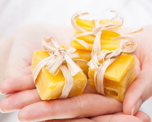 Unrecognizable woman's hands holding pieces of natural beeswax, packed and decorated