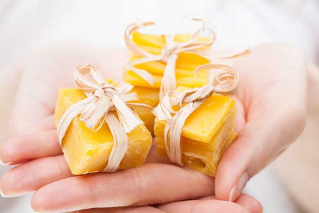 Unrecognizable woman's hands holding pieces of natural beeswax, packed and decorated